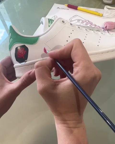 Une participante peint une rose sur le talon de sa Stan Smith pendant l'atelier custom