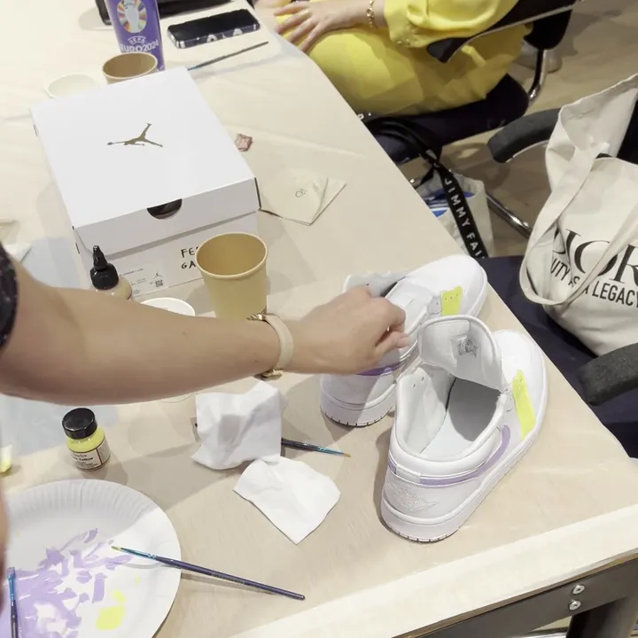 Mains qui peignent une sneaker blanche, palette et pinceaux sur la table