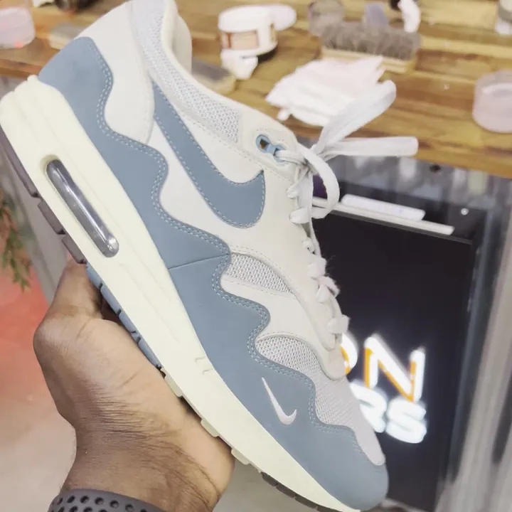 Une sneaker tenue à la main devant le stand Maison Sneakers